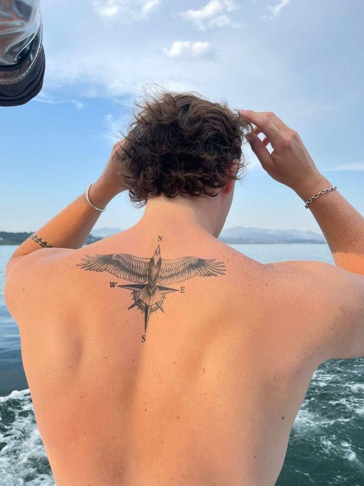 Eagle and compass tattoo with N, E, S, W letters on the upper back of a man on a boat