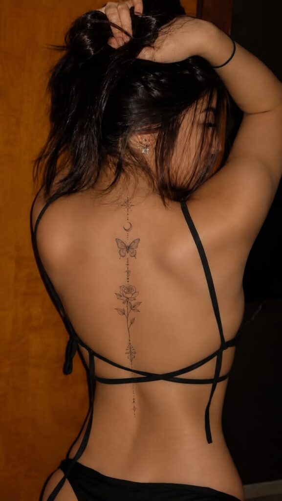 Delicate spine tattoo with a crescent moon, butterfly, rose and dotted line on a woman’s back