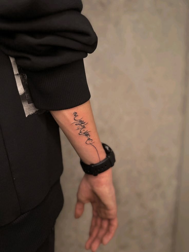 Abstract calligraphy script tattoo flowing down the forearm of a man wearing a black watch