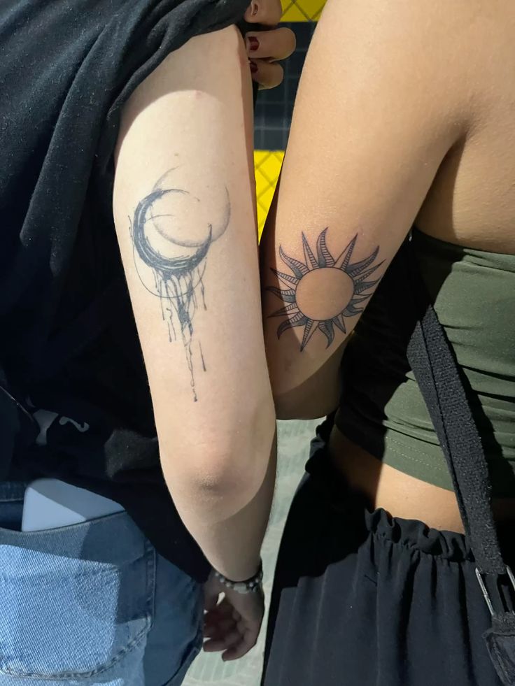 Matching upper arm tattoos of a dripping crescent moon and a bold sun with pointed rays
