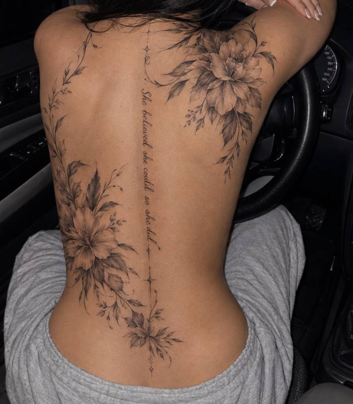 Large floral back tattoo with peonies, leaves and a script line running down the spine