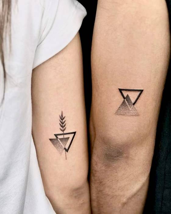 Matching geometric triangle tattoos with dotwork shading and a small leaf on two upper arms