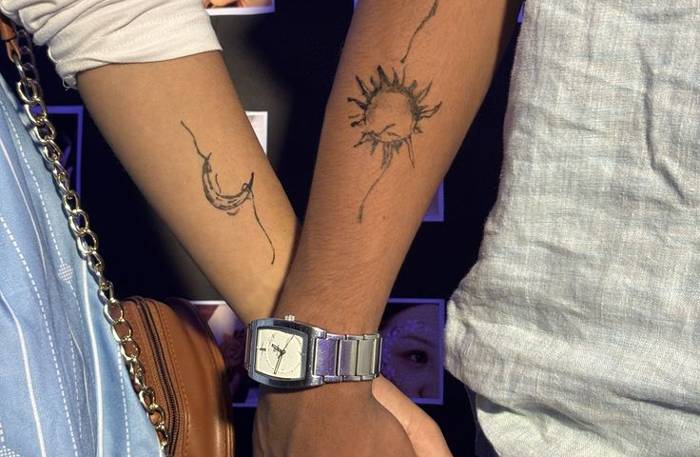 Hand-drawn style sun and crescent moon tattoos on the forearms of a couple holding hands
