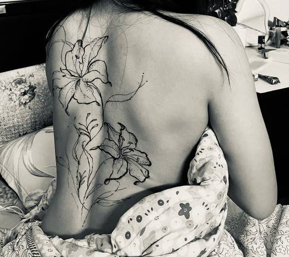 Fine-line lily flowers with stems tattooed down the upper back