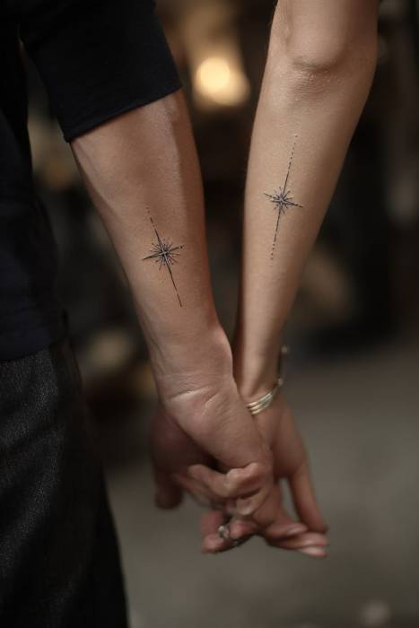 Two matching fine-line star tattoos on the forearms of a couple holding hands