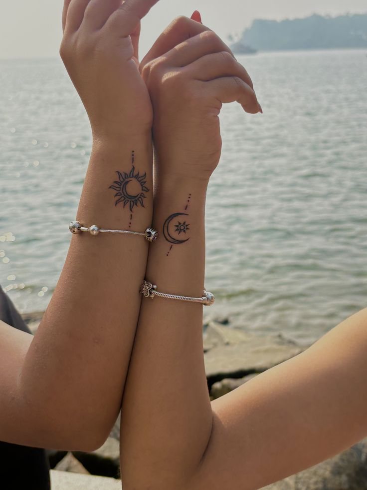 Matching wrist tattoos of a moon inside a sun and a sun inside a crescent moon