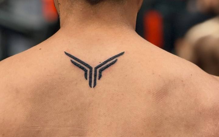 Minimal bold black wing shapes tattooed on the upper back below the neck
