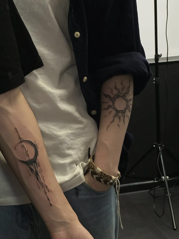 Dark crescent moon with vines on one forearm and a branch-like sun on the other arm