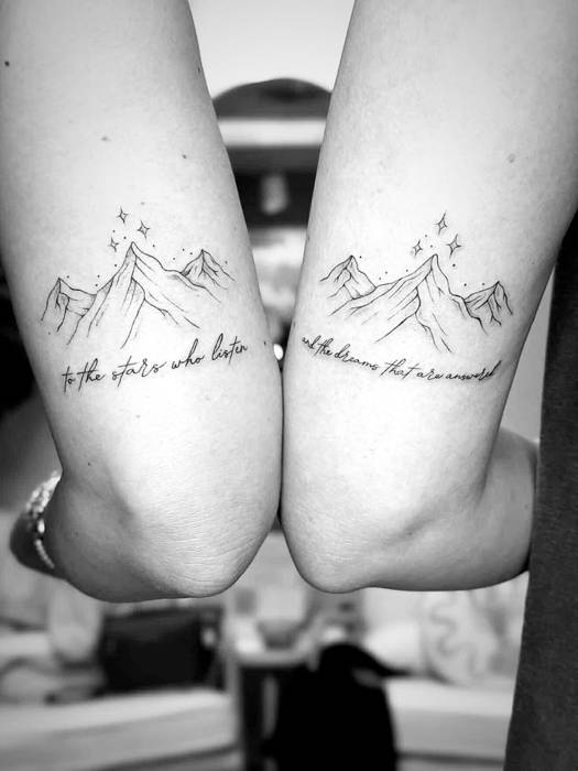 Matching mountain tattoos with stars and a handwritten quote across two arms