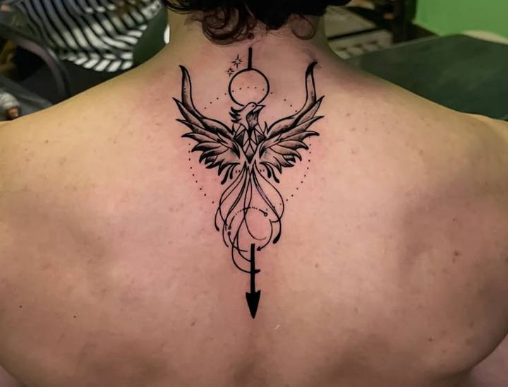 Phoenix with an arrow, circle and dotted details tattooed on the upper back