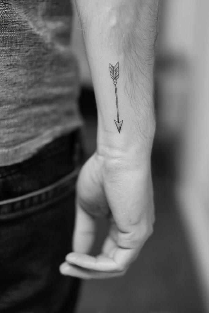 Black and white photo of a small arrow tattoo on the inner forearm of a man