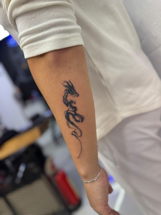Small black ink-brush dragon tattoo on the forearm of a man with a silver bracelet