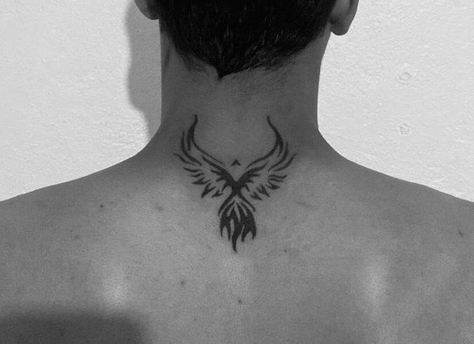 Small black phoenix tattoo with spread wings on the back of the neck