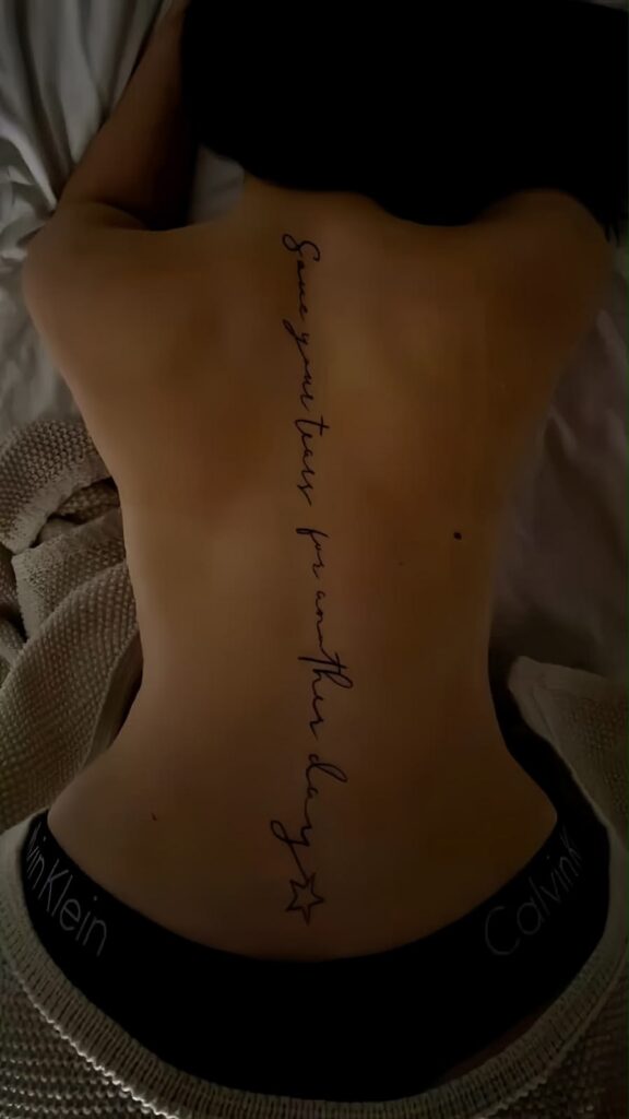 Cursive spine tattoo quote reading ‘save your tears for another day’ ending with a small star