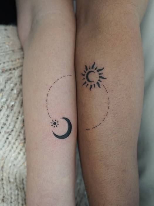 Matching sun and crescent moon tattoos connected by a dotted orbit line across two forearms