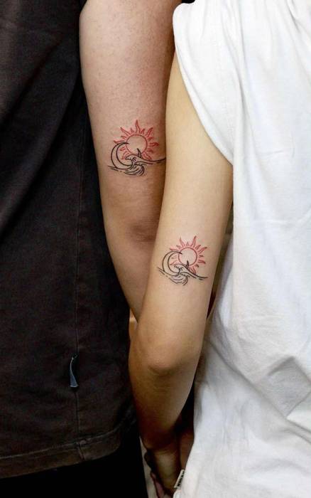 Matching red sun and black wave tattoos with a crescent moon on the upper arms of a couple