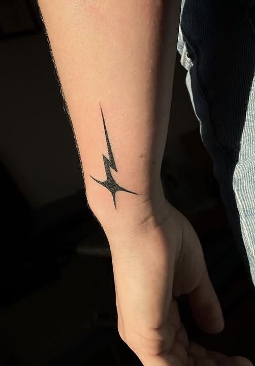 Black tribal lightning bolt tattoo with sharp points on the inner forearm near the wrist