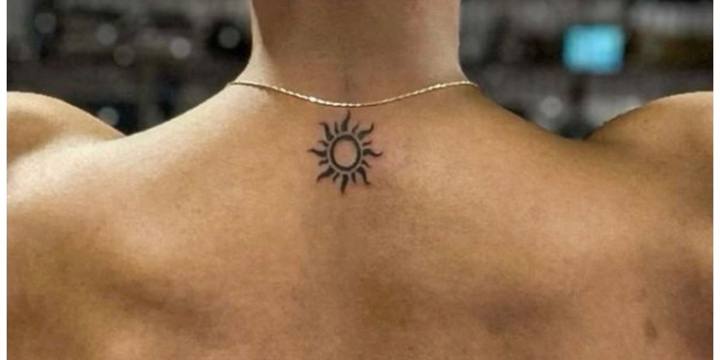 Small tribal sun tattoo at the base of the neck under a thin gold chain