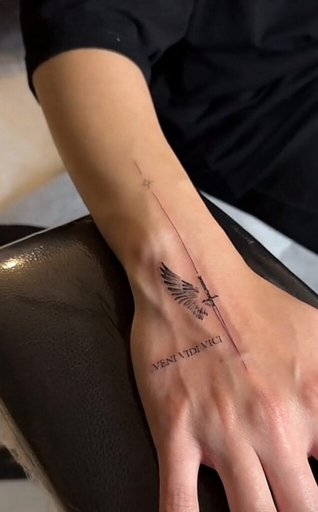 Small wing and sword tattoo with the Latin words veni vidi vici on the hand and wrist