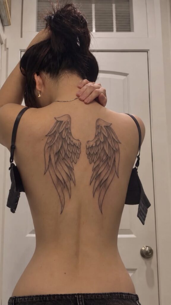 Angel wings back tattoo across the shoulder blades of a woman with her hair in a bun