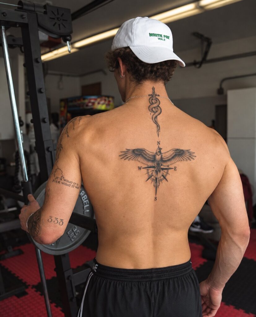 Man in a gym with an eagle and compass tattoo on his upper back and a sword and snake tattoo on his neck