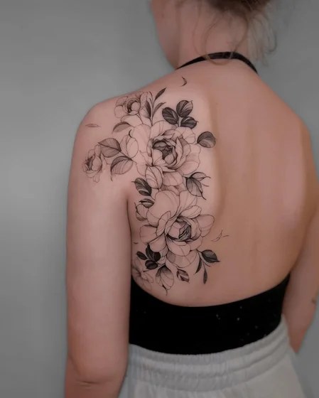 Fine-line flower and leafy vine tattoo winding around a woman’s upper arm and shoulder
