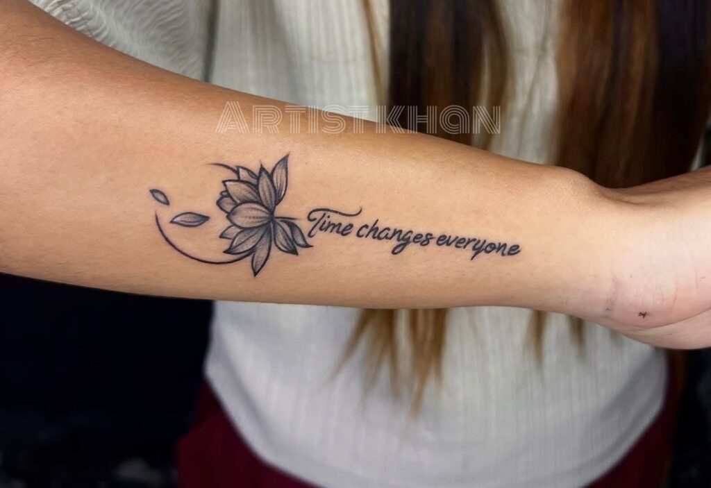 Shaded lotus flower with falling petals and a script quote along the forearm