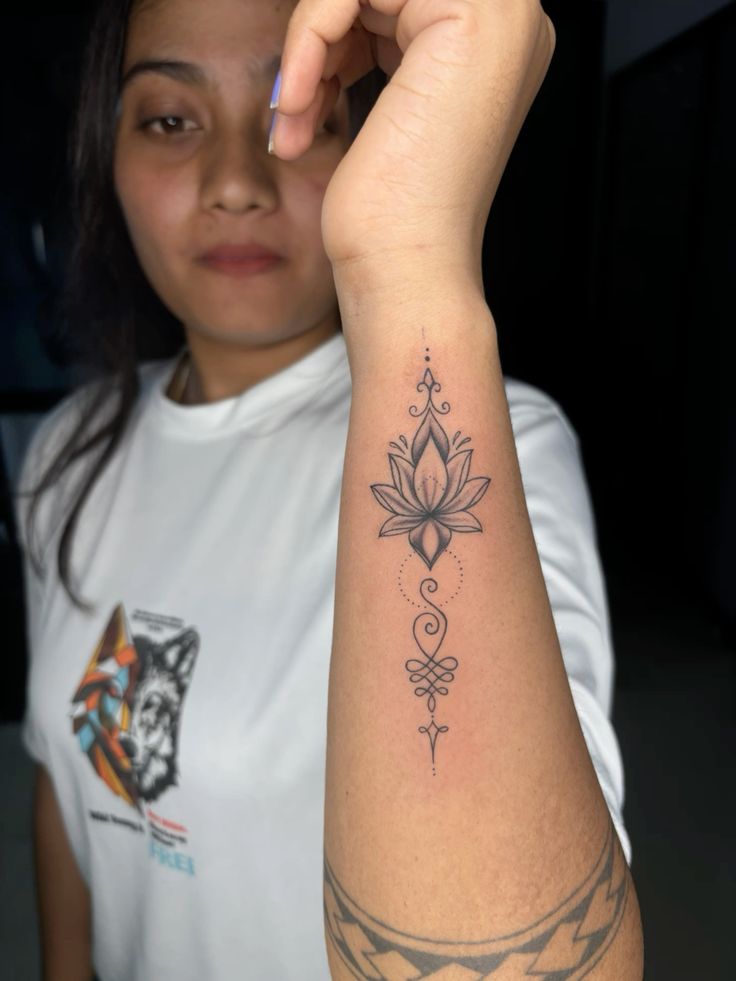 Fine-line lotus flower with an unalome spiral and dots on the inner forearm