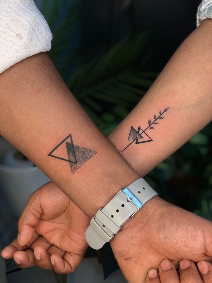 Matching forearm tattoos of overlapping triangles with dotwork shading and a small leafy branch