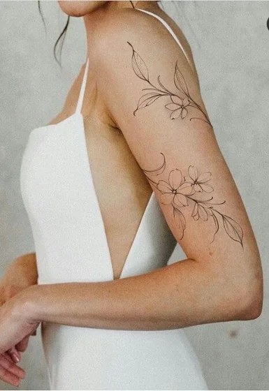 Black and white photo of large peony tattoos on both shoulder blades with an ornamental line down the spine