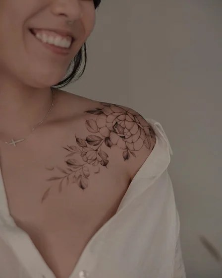 Black and grey peony and leaf cluster tattoo on a woman’s shoulder blade
