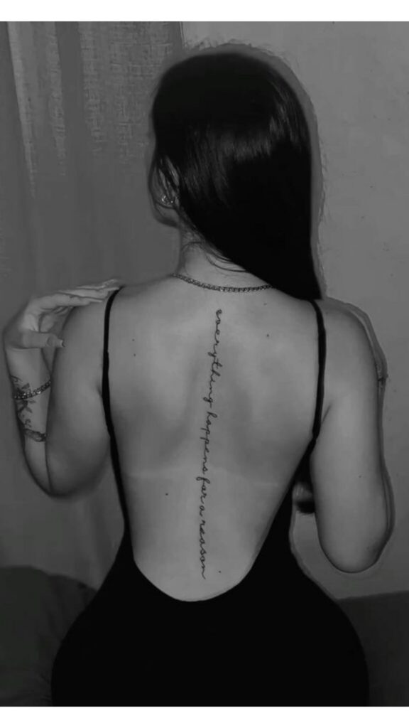 Black and white photo of a woman with a cursive spine tattoo reading ‘everything happens for a reason