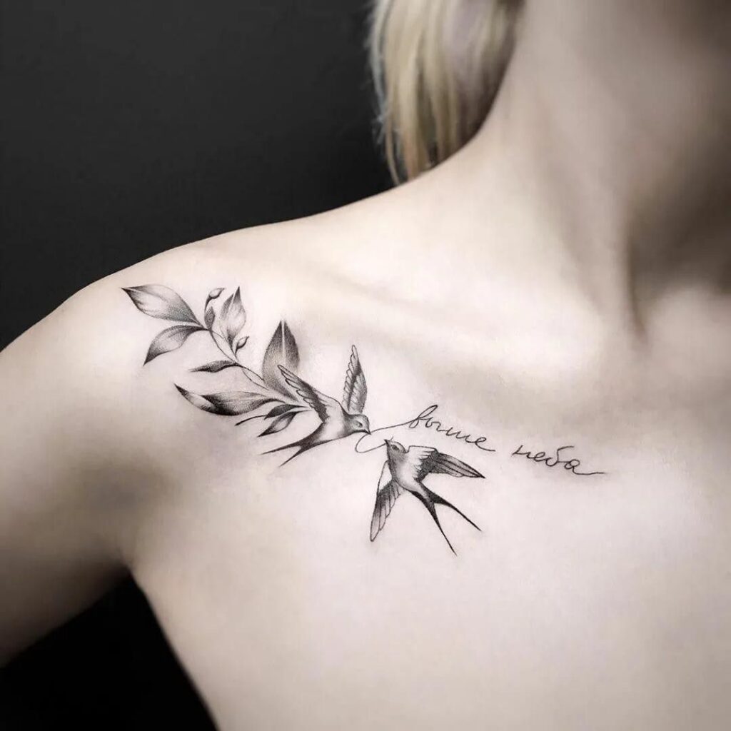 Two swallows with a leafy branch and a cursive Russian phrase tattoo on the collarbone and shoulder